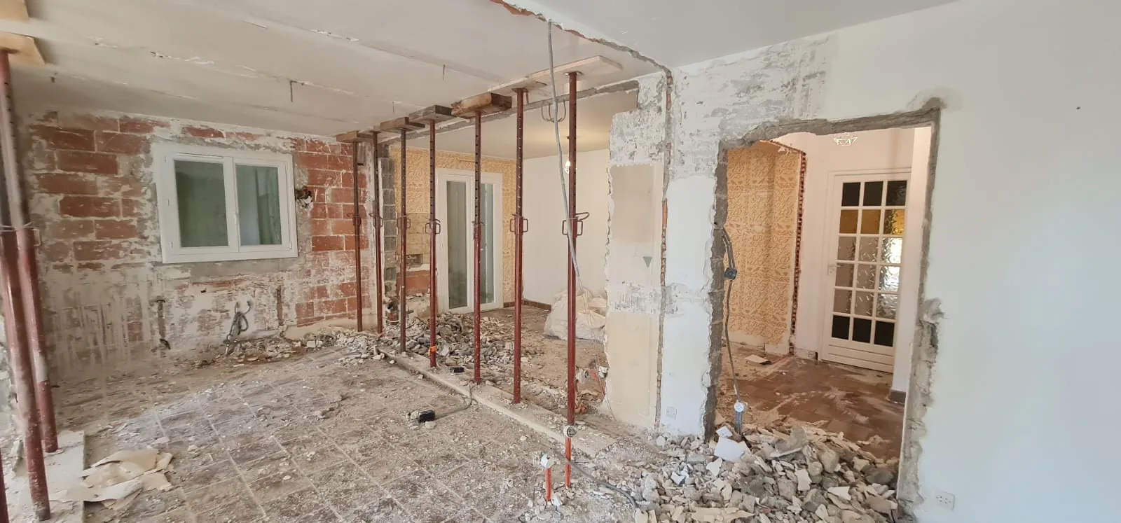 Étaiement du plancher par étais métalliques devant un mur en briques avant ouverture