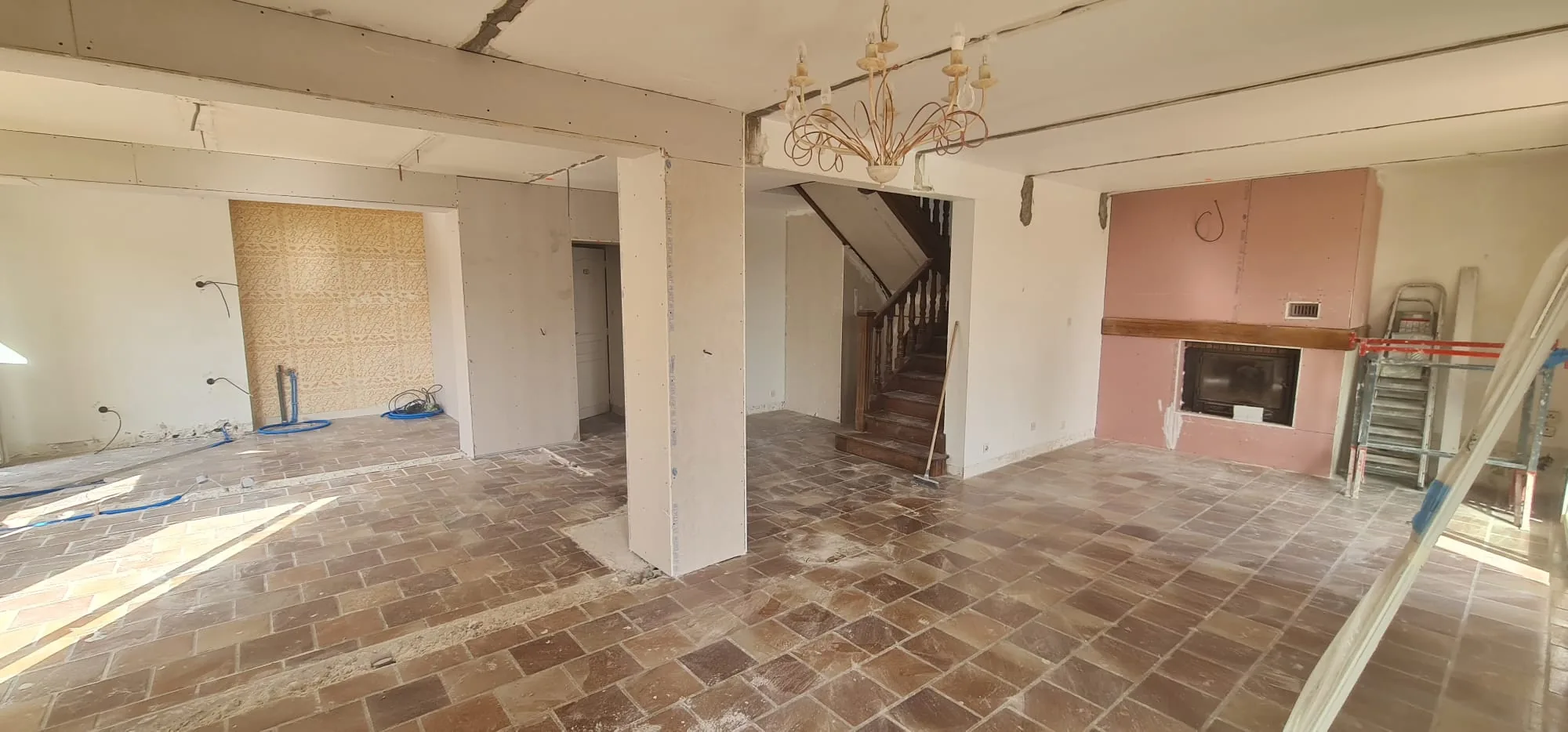 Pièce de vie ouverte avec cheminée et escalier en bois après ouverture des murs