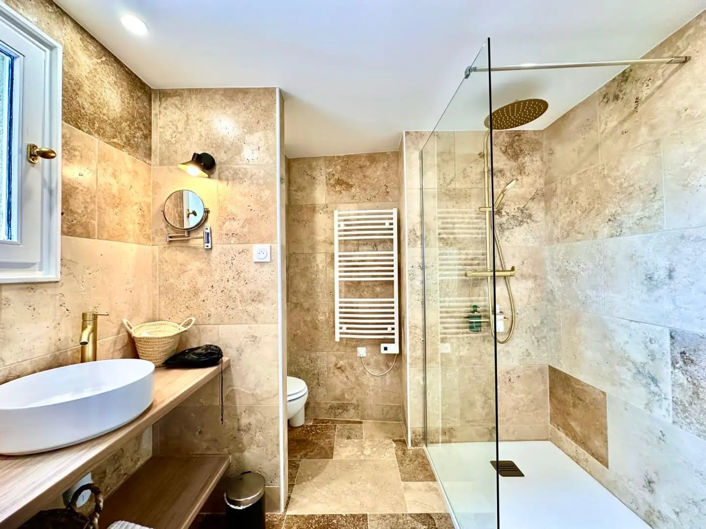 Salle de bain rénovée en travertin naturel avec douche à l'italienne et robinetterie dorée — maison en Provence