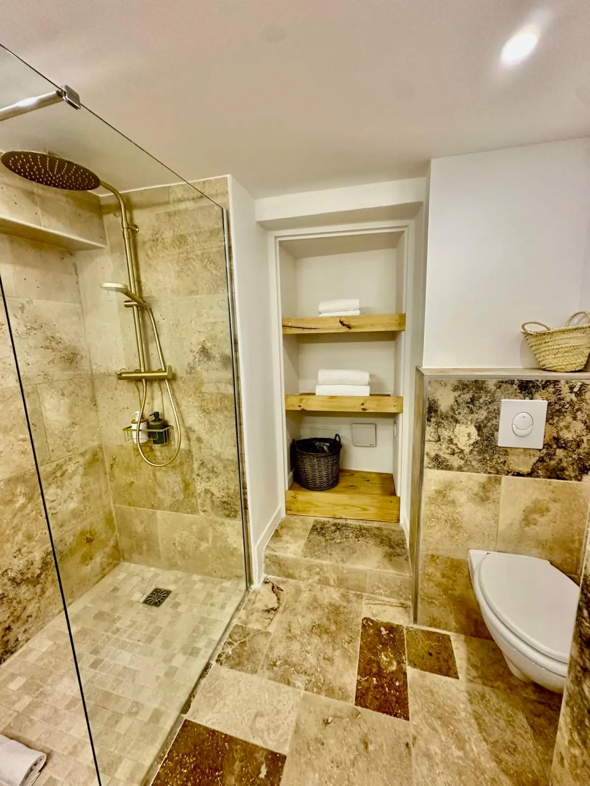Après rénovation — douche à l'italienne en mosaïque de travertin, niche avec étagères en bois massif et WC suspendu
