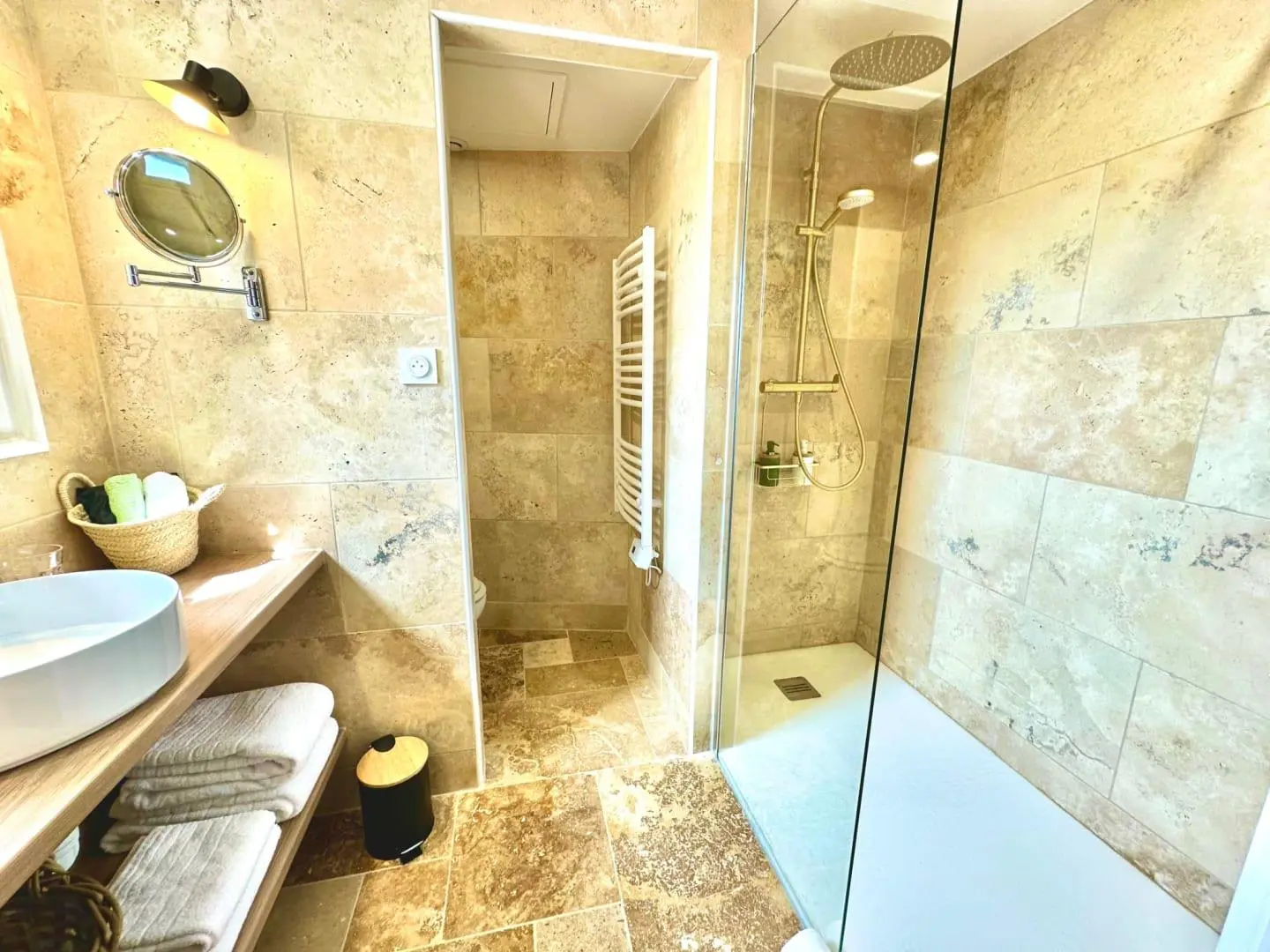 Après rénovation — salle de bain en travertin avec vasque à poser, WC en alcôve, sèche-serviettes et douche à l'italienne