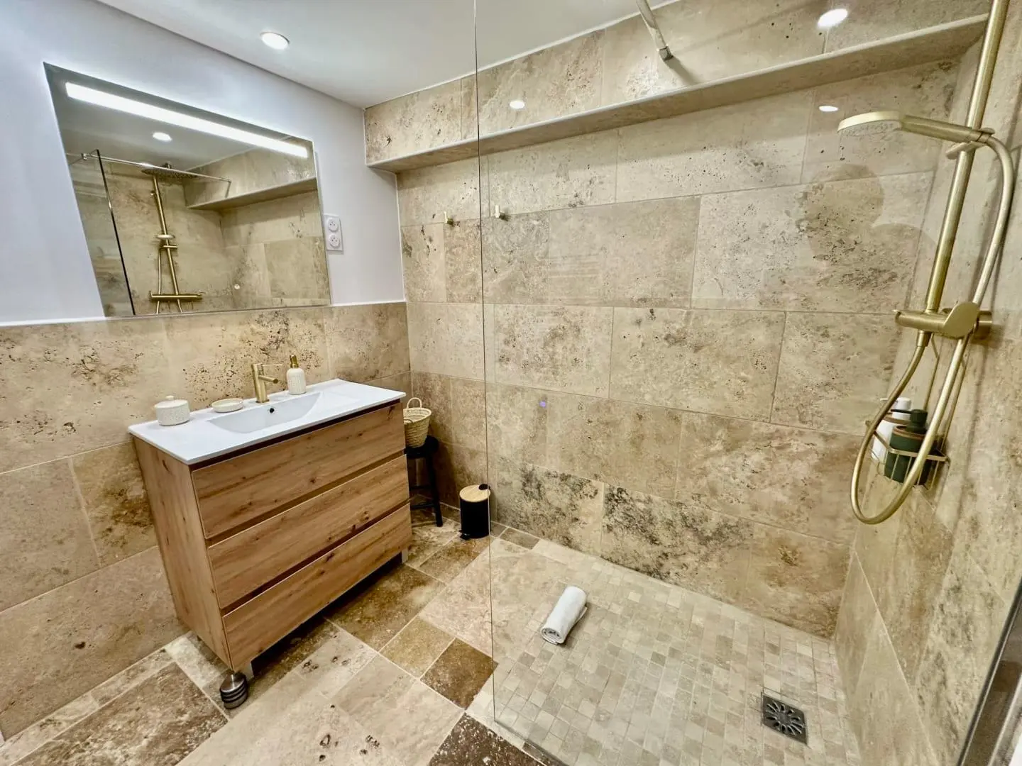 Douche à l'italienne avec sol en mosaïque de travertin, meuble vasque en chêne et colonne de douche dorée, salle de bain en Provence