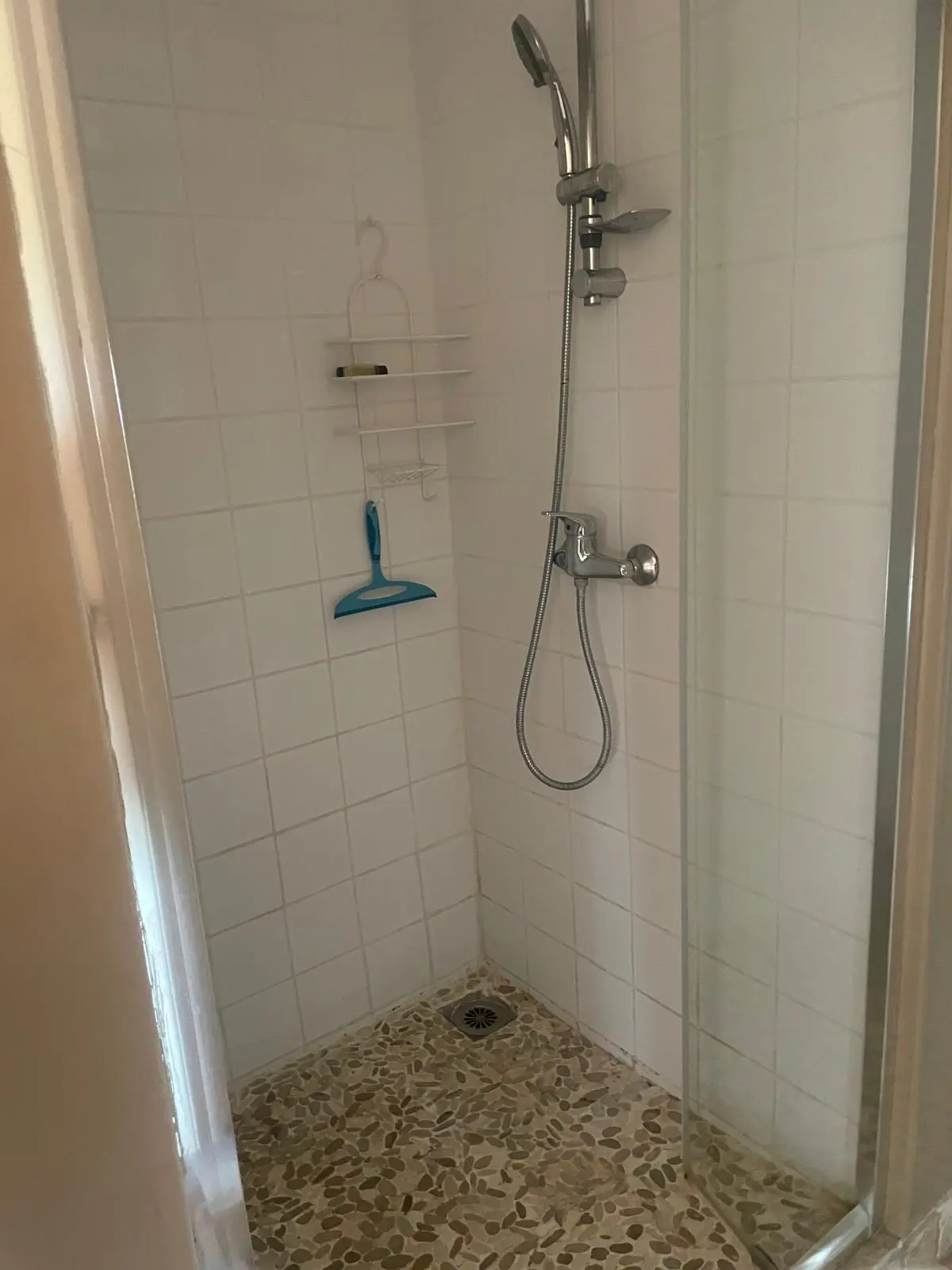 Avant rénovation — douche carrelée blanche avec receveur en galets et robinetterie chromée