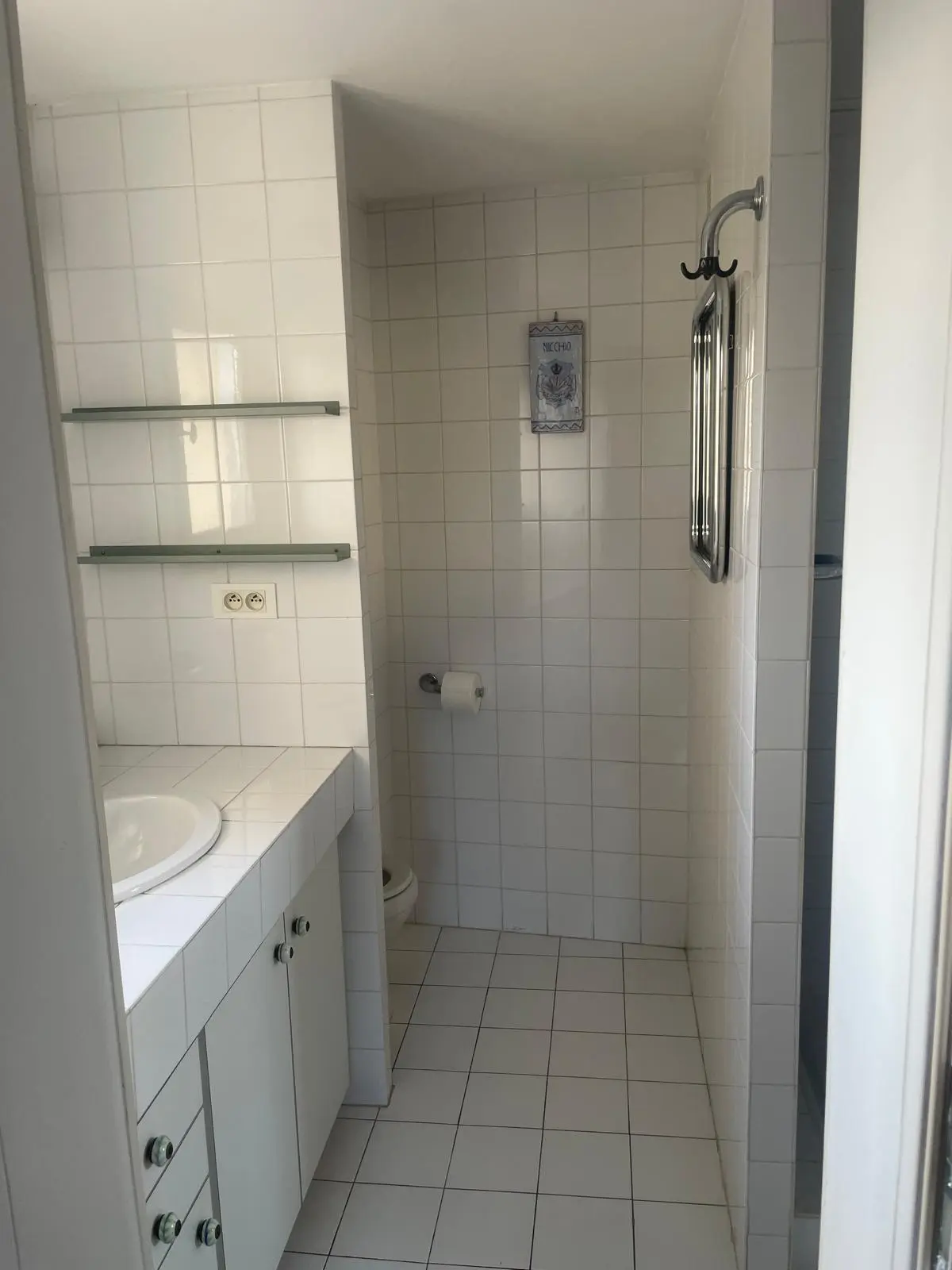 Avant rénovation — salle de bain en faïence blanche avec plan vasque maçonné, étagères et WC en alcôve